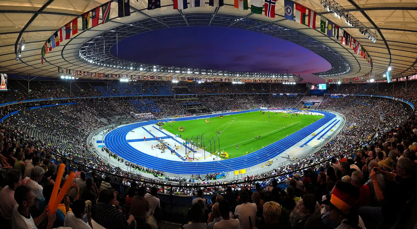 Olympiastadion in Berlin at night, full stands around the blue track