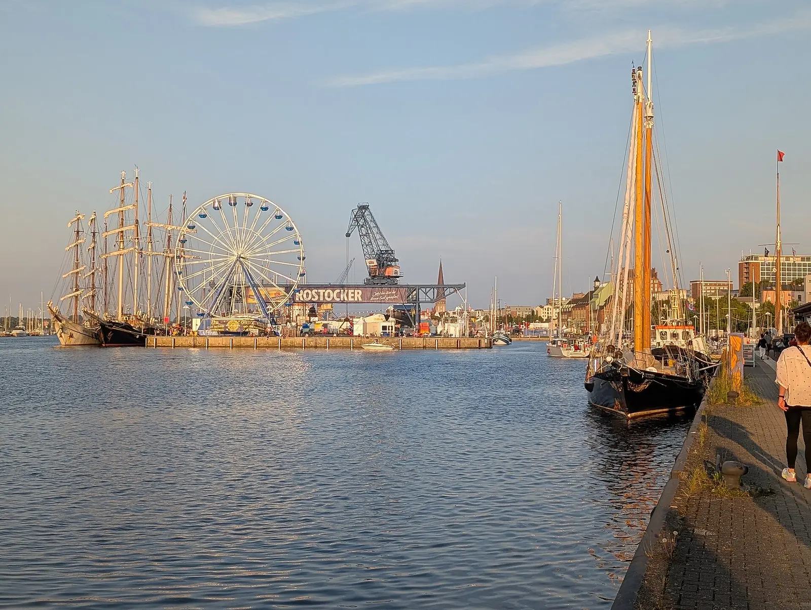 Tall ships moored in Rostock harbour at golden hour with a Ferris wheel behind